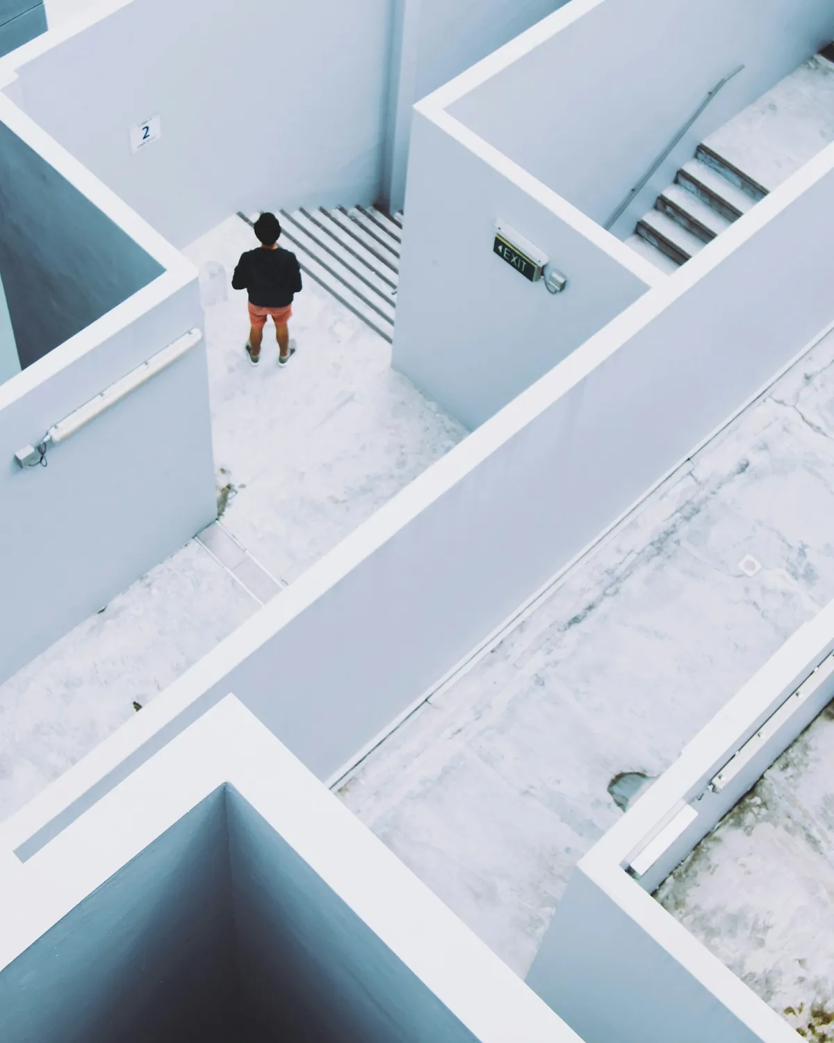 A person standing in a maze of white walls and staircases, seen from above